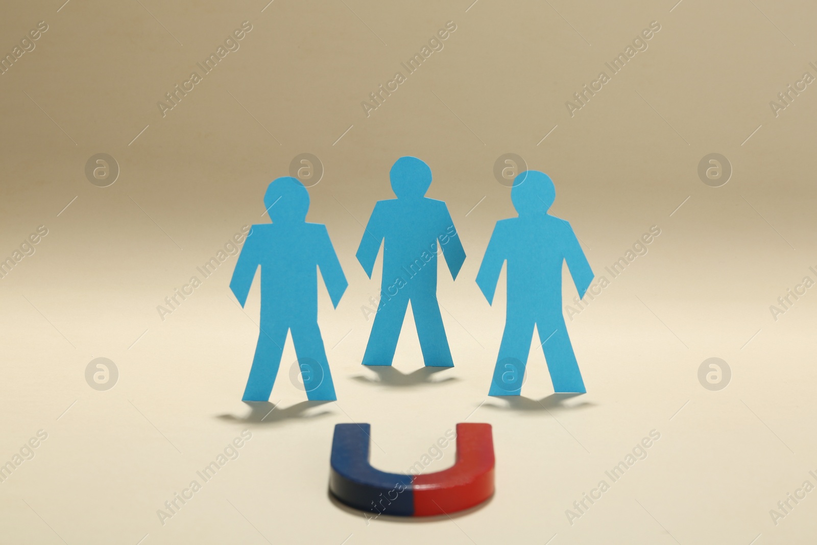 Photo of Magnet attracting paper people on beige background