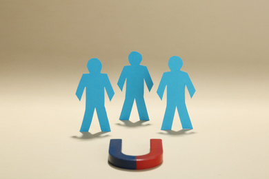 Magnet attracting paper people on beige background