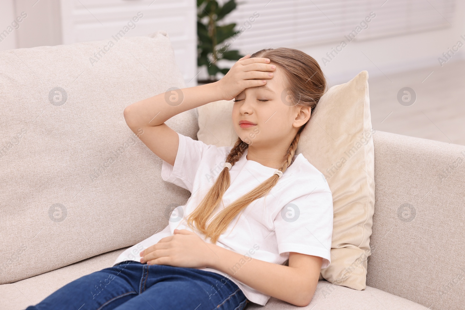 Photo of Little girl suffering from headache on sofa indoors