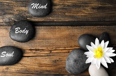 Photo of Flat lay composition of lotus flower and stones with words Mind, Body, Soul on wooden background, space for text. Zen lifestyle