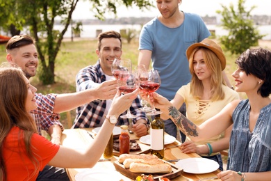 Photo of Young people with glasses of wine at table outdoors. Summer barbecue