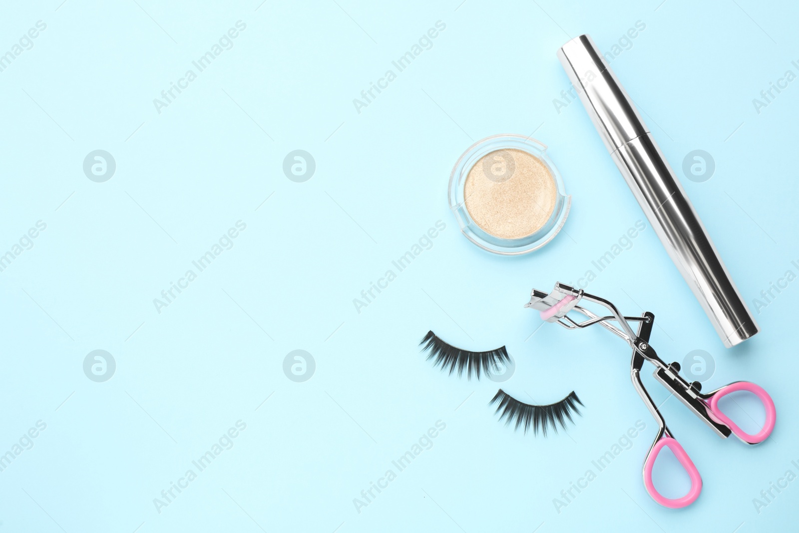 Photo of Eyelash curler and makeup products on light blue background, flat lay. Space for text