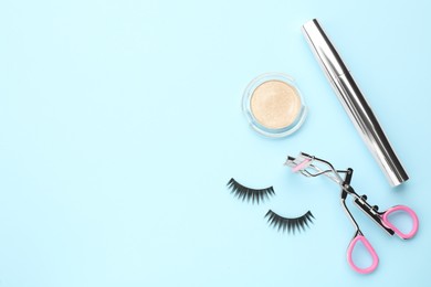 Photo of Eyelash curler and makeup products on light blue background, flat lay. Space for text