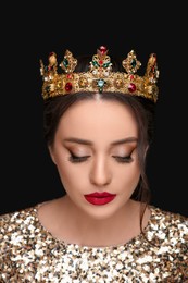 Beautiful young woman wearing luxurious crown on black background