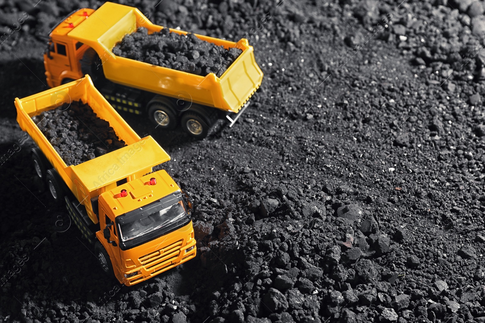 Image of Toy tipper trucks with coal in field. Space for text