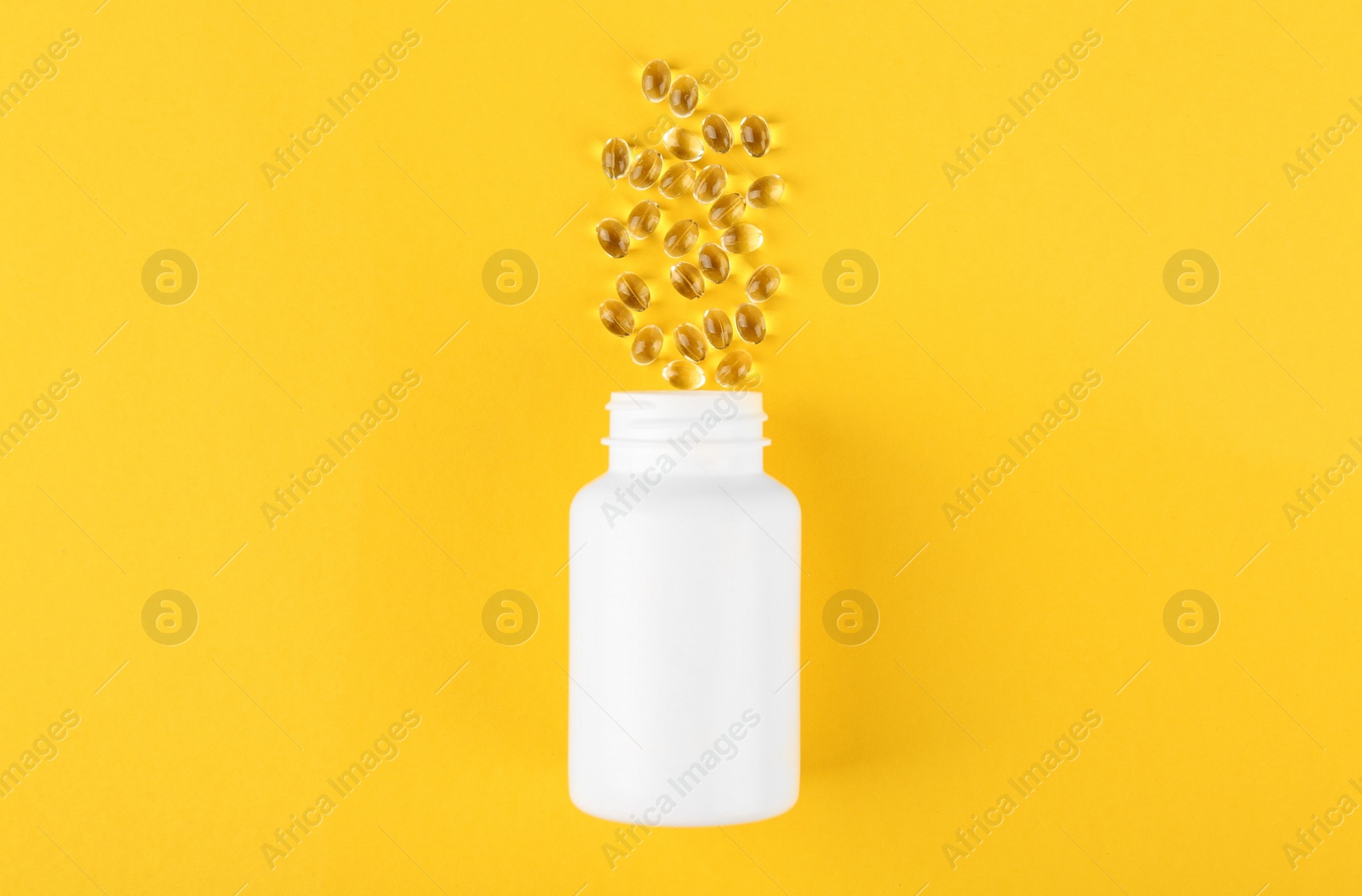 Photo of White medical bottle and vitamin capsules on yellow background, top view