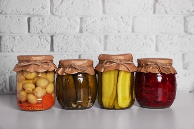 Many glass jars with different preserved vegetables and mushrooms on light grey table