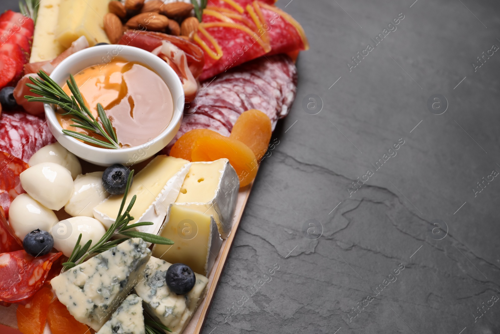 Photo of Wooden plate with different delicious snacks on black table, above view. Space for text