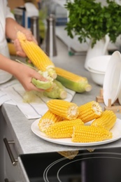 Photo of Plate with ripe corn cobs and blurred woman on background