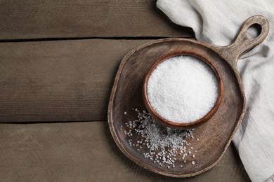 Photo of Bowl of natural sea salt on wooden table, top view. Space for text