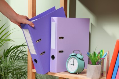 Woman taking binder office folder from shelving unit indoors, closeup