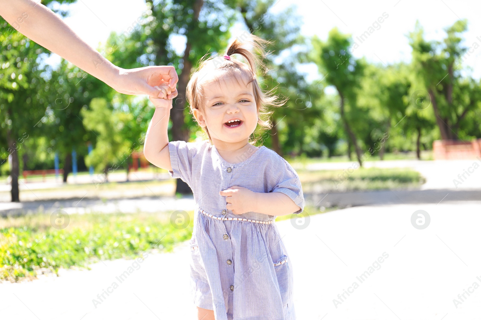 Photo of Adorable baby girl holding mother's hand while learning to walk outdoors