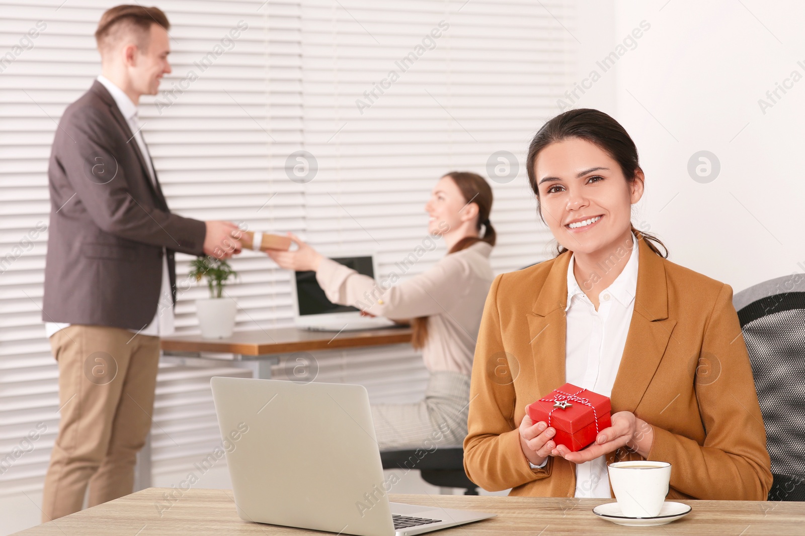 Photo of Happy woman holding festive box and man presenting gift to his colleague in office