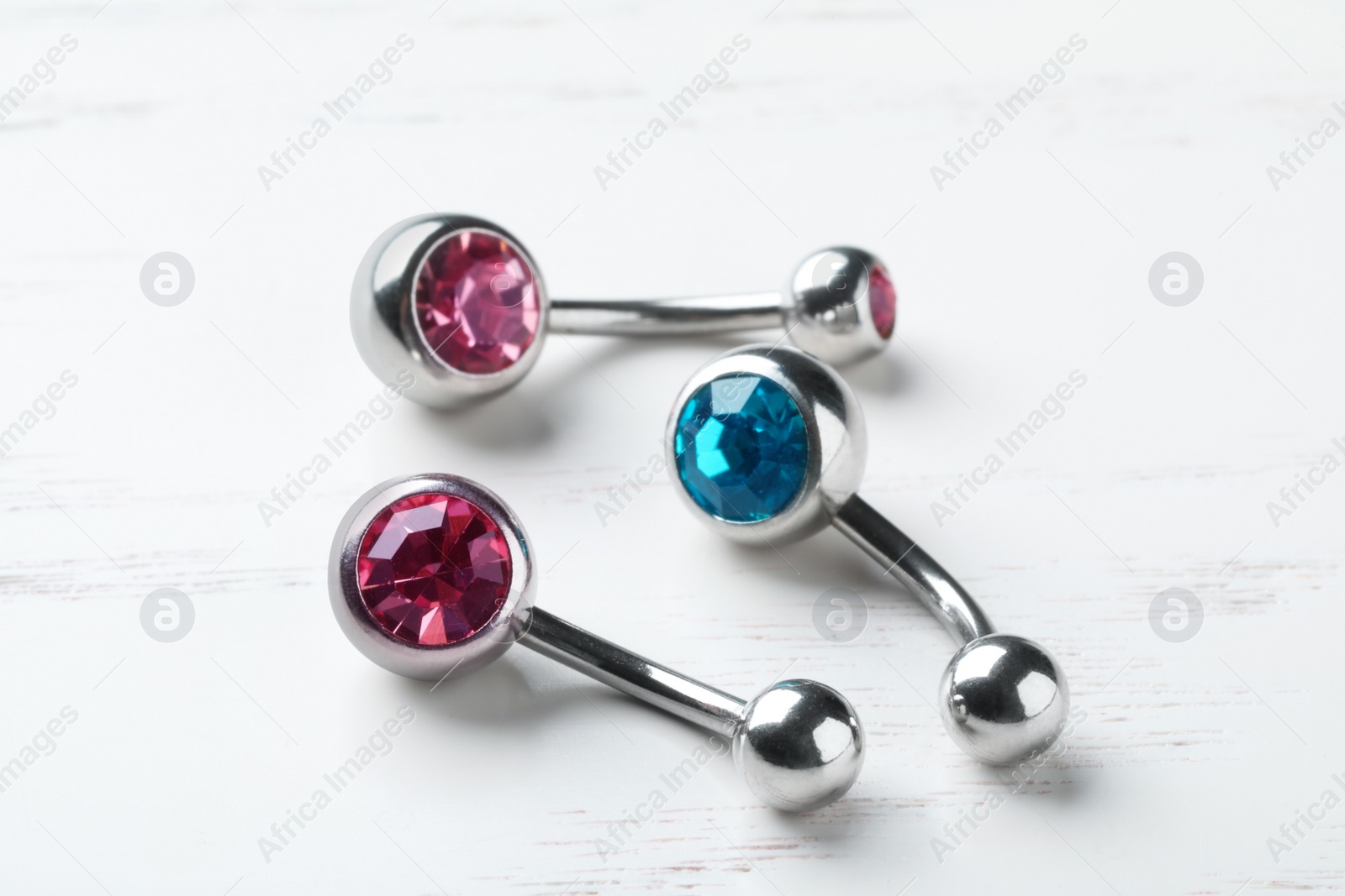 Photo of Stylish navel barbells on white wooden table, closeup. Piercing jewelry