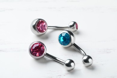 Stylish navel barbells on white wooden table, closeup. Piercing jewelry