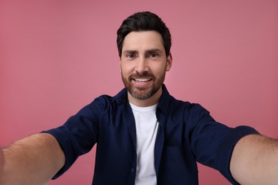 Smiling man taking selfie on pink background