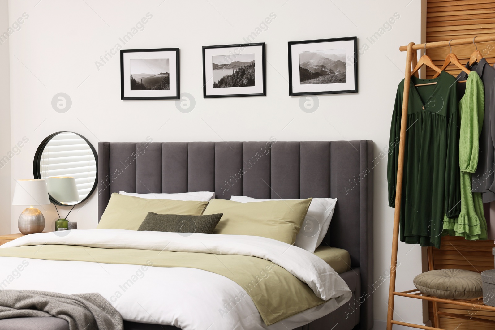 Photo of Comfortable bed and clothes on rack in stylish room