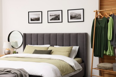 Comfortable bed and clothes on rack in stylish room