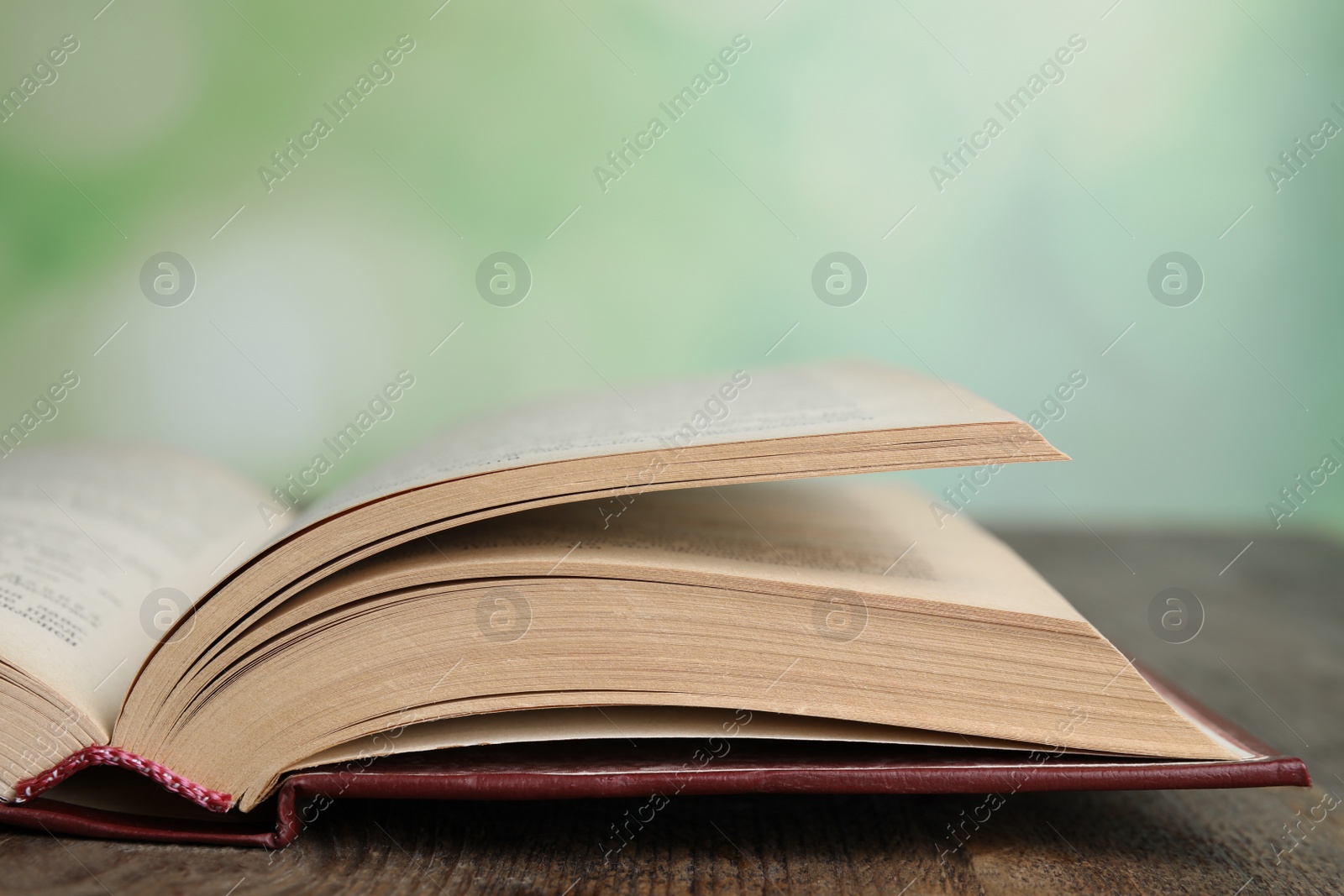 Photo of Open book on wooden table against blurred green background, closeup