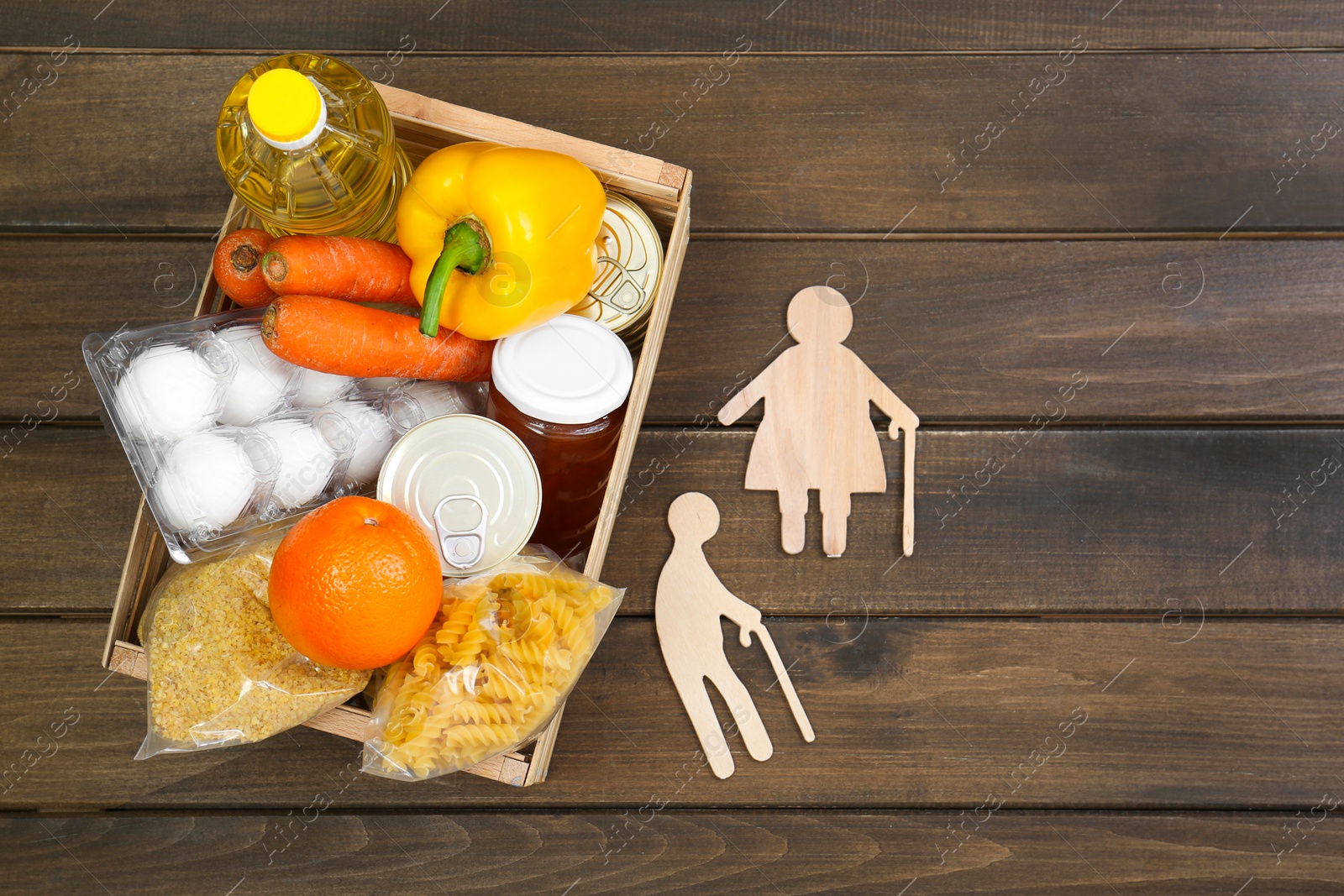 Photo of Humanitarian aid for elderly people. Crate with donation food and figures of couple on wooden table, top view