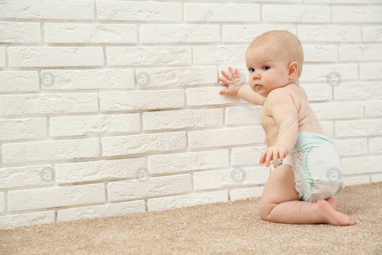 Photo of Cute little baby crawling on carpet near brick wall, space for text