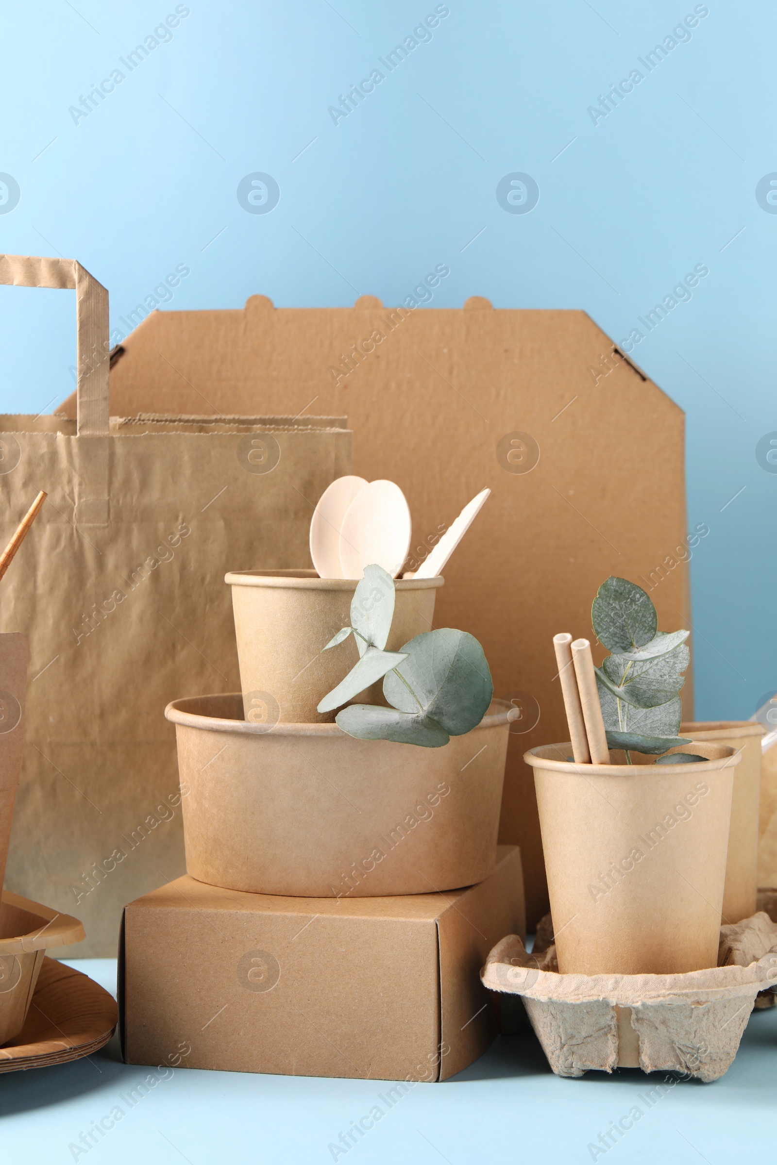 Photo of Eco friendly food packaging. Paper containers, tableware, bag and eucalyptus branches on white table against light blue background