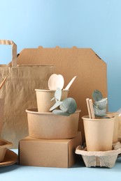 Photo of Eco friendly food packaging. Paper containers, tableware, bag and eucalyptus branches on white table against light blue background