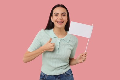 Photo of Happy young woman with blank white flag showing thumbs up on pink background. Mockup for design