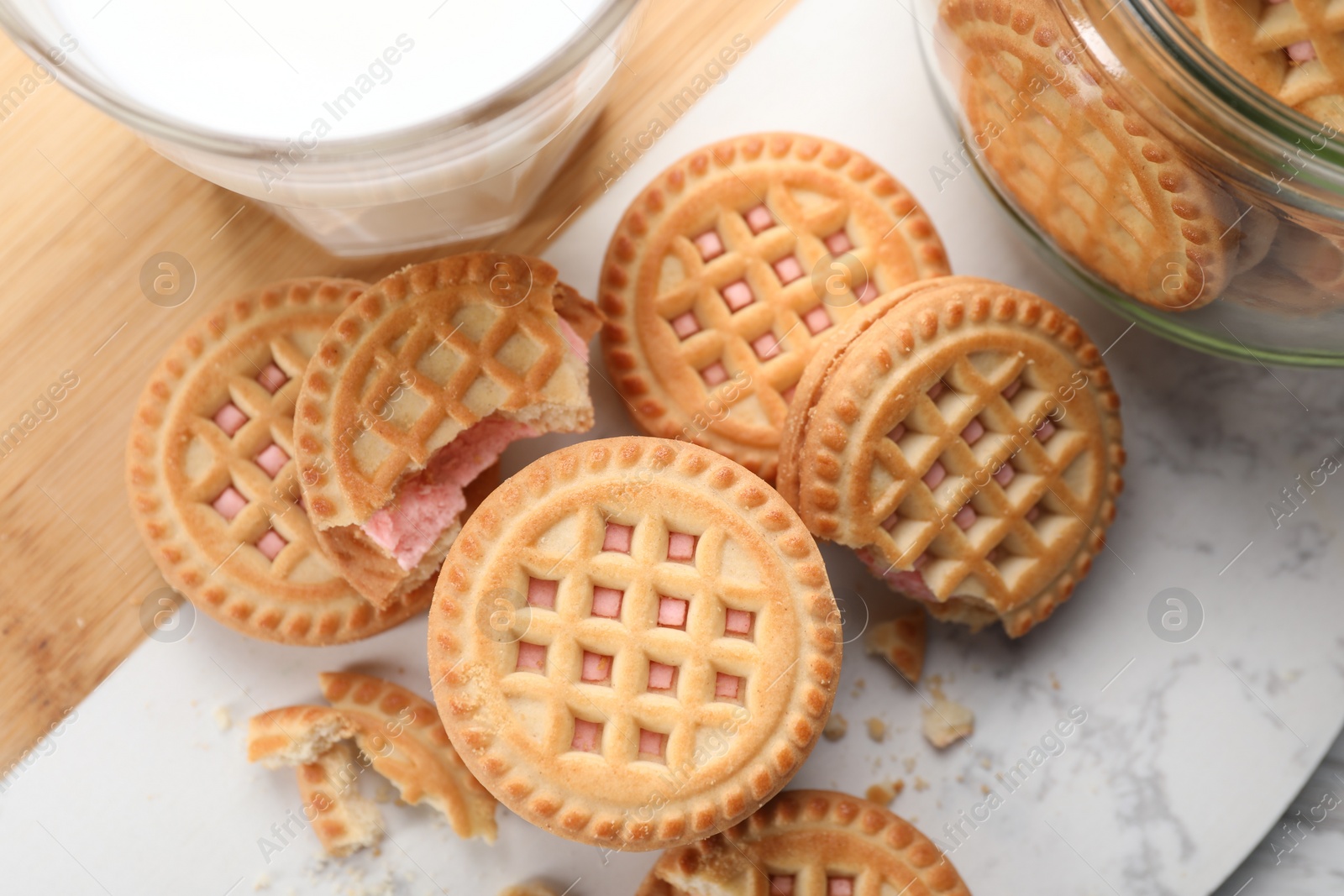 Photo of Tasty sandwich cookies with cream and glass of milk on white marble board, flat lay