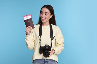 Photo of Happy woman with passport, tickets and camera on light blue background