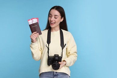 Happy woman with passport, tickets and camera on light blue background