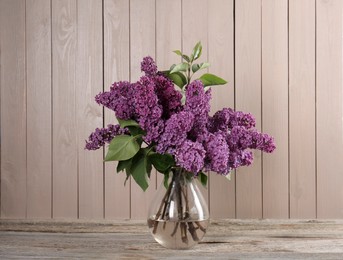 Photo of Beautiful lilac flowers in vase on wooden table