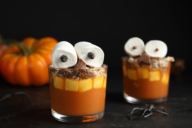Photo of Glasses with delicious dessert decorated as monsters on black table. Halloween treat