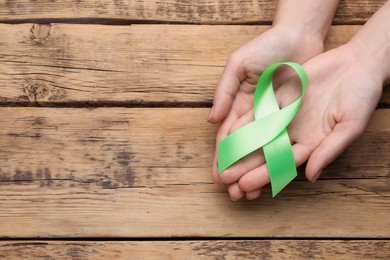 World Mental Health Day. Woman holding green ribbon on wooden background, top view with space for text