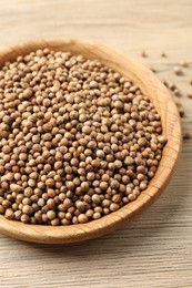 Dried coriander seeds in bowl on wooden table, closeup