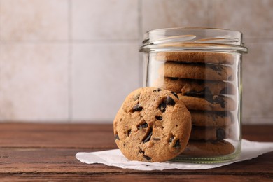 Photo of Glass jar with delicious chocolate chip cookies on wooden table. Space for text