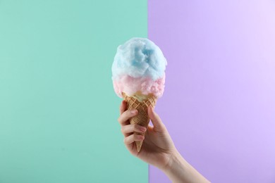 Photo of Woman holding waffle cone with cotton candy on color background, closeup