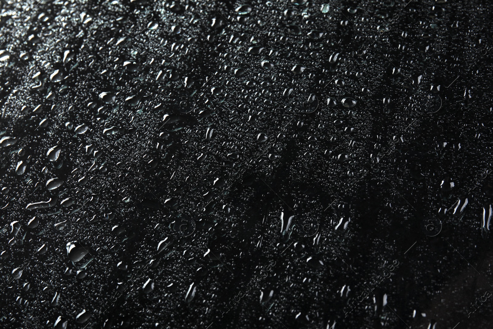 Photo of Glass with rain drops against dark background