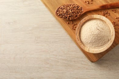 Photo of Bowl of buckwheat flour and spoon with grains on white wooden table, flat lay. Space for text