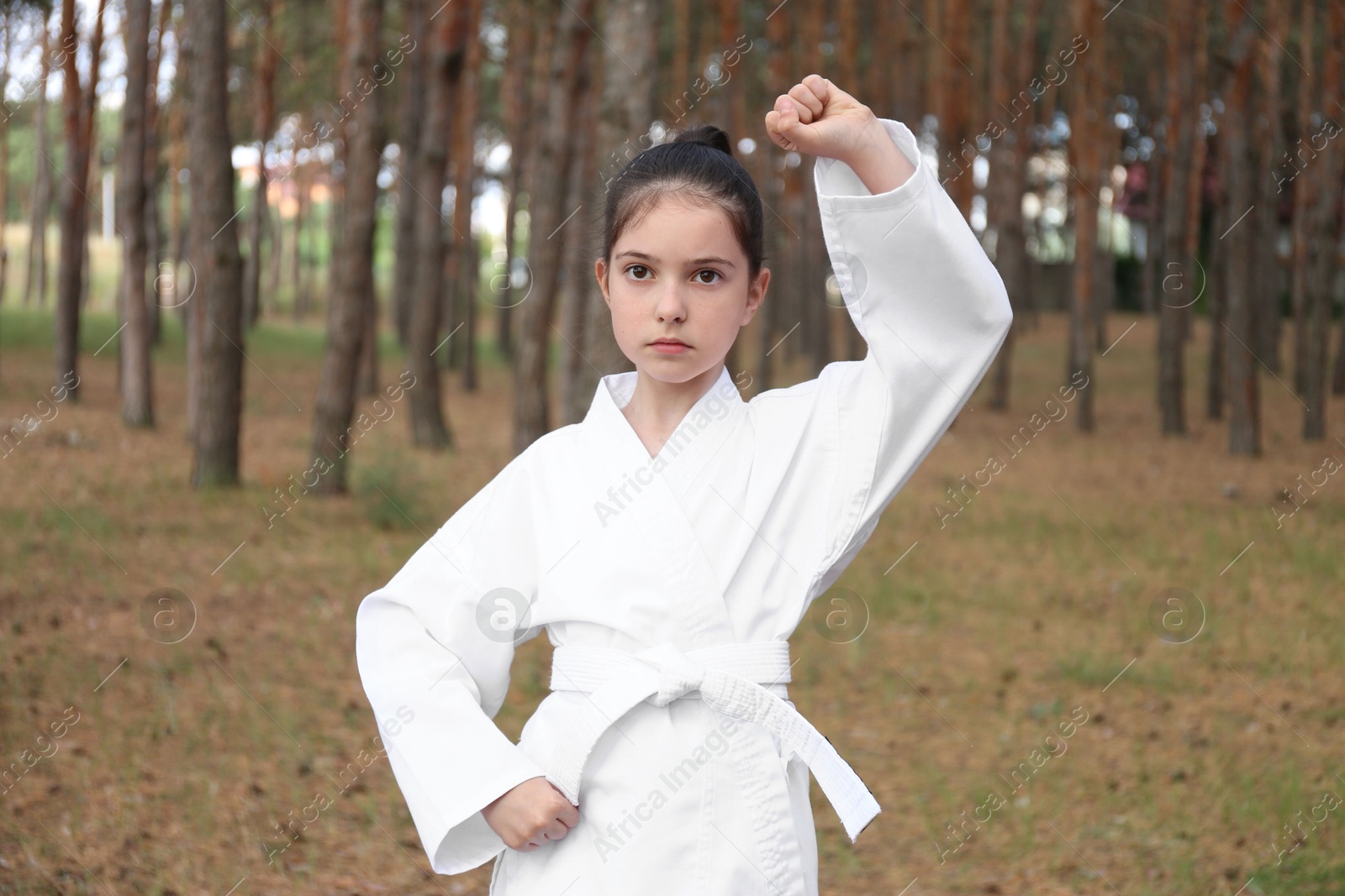 Photo of Cute little girl in kimono practicing karate in forest