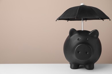 Photo of Small umbrella and piggy bank on white table. Space for text