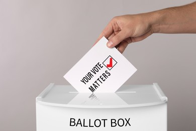 Man putting paper with text Your Vote Matters and tick into ballot box on light grey background