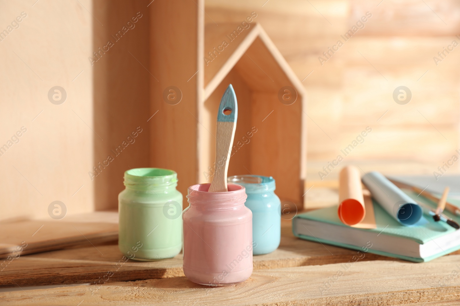 Photo of Jars of paints with brush on wooden table, closeup. Interior elements