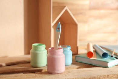 Photo of Jars of paints with brush on wooden table, closeup. Interior elements