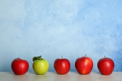 Photo of Row of red apples with green one on table. Be different
