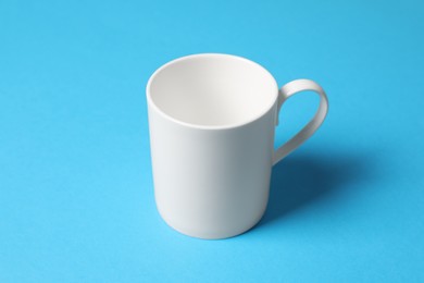 Photo of One white ceramic mug on light blue background