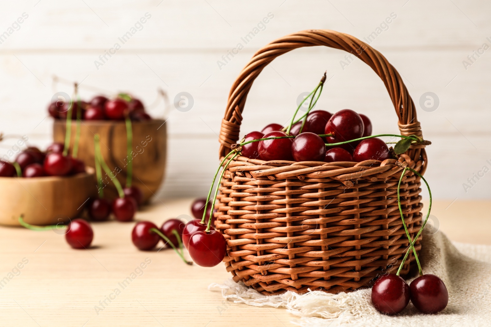 Photo of Wicker basket of delicious cherries on wooden table against white background, space for text