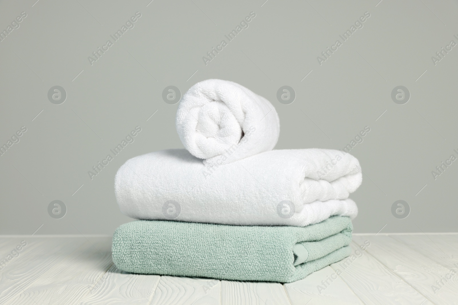 Photo of Soft towels on white wooden table against light grey background