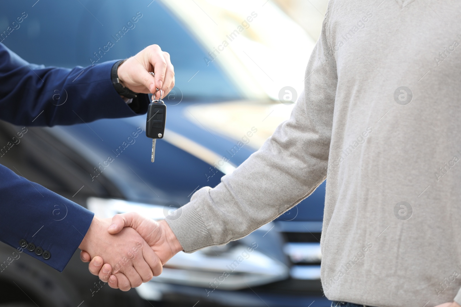 Photo of Salesman giving key to customer while shaking hands in modern auto dealership, closeup. Buying new car