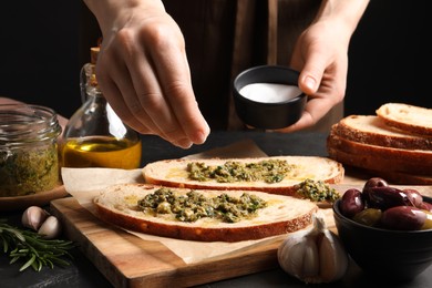 Photo of Woman salting tasty bruschettas with pesto at table, closeup